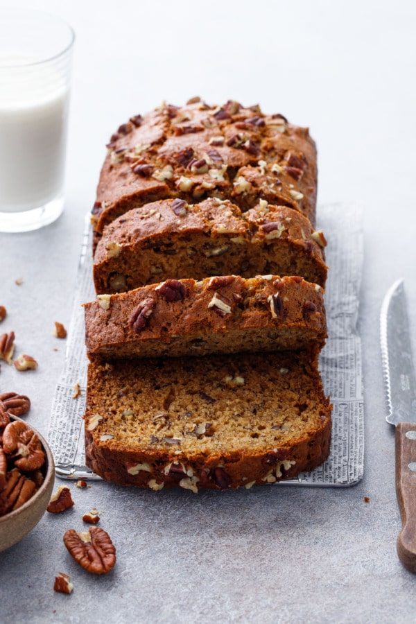 Sliced Bananas Foster Banana Bread with knife and pecans and a glass of milk