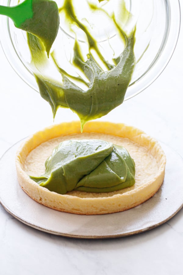 Pouring thick green matcha pastry cream into a pre-baked tart shell
