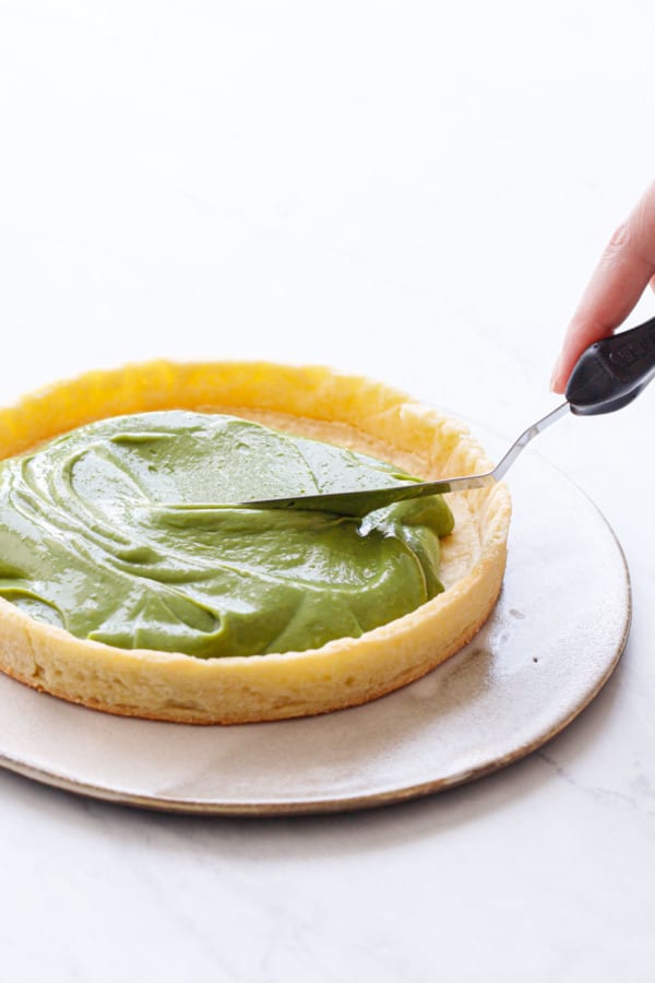 Spreading green matcha pastry cream into a pre-baked tart shell