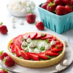 Matcha Strawberry Tart on a marble background, with turquoise basket of strawberries and a bowl of mini meringue kisses.