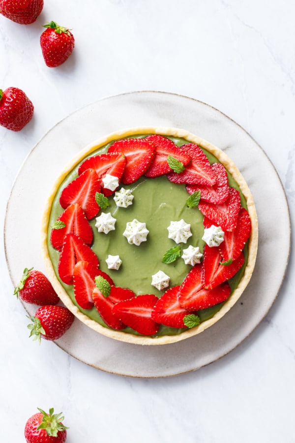 Overhead of green matcha pastry cream-filled tart with a ring of overlapping strawberry slices, and tiny white meringue kisses for decoration.