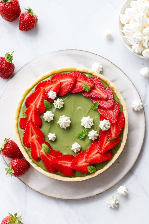 Overhead shot showing green matcha tart with a ring of overlapping strawberry slices, and tiny white meringue kisses for decoration.