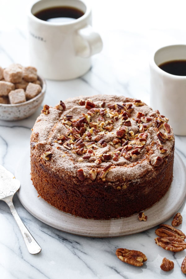 Greek Yogurt Coffee Cake on a ceramic plate with coffee cups and sugar cubes in the background.