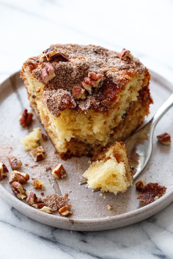 Fork with a bite of coffee cake on a ceramic plate with chopped pecans scattered around