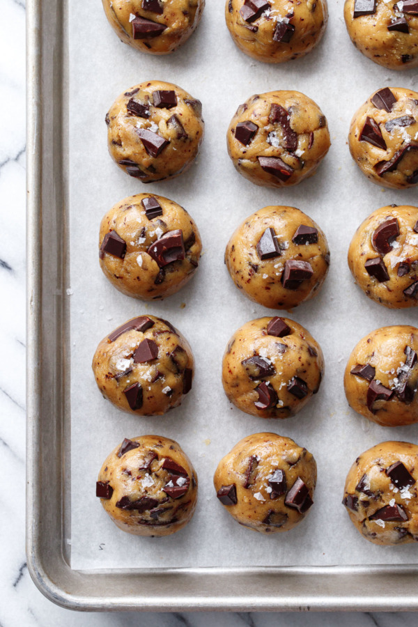 Balls of olive oil chocolate chip cookie dough in neat rows on a parchment-lined cookie sheet