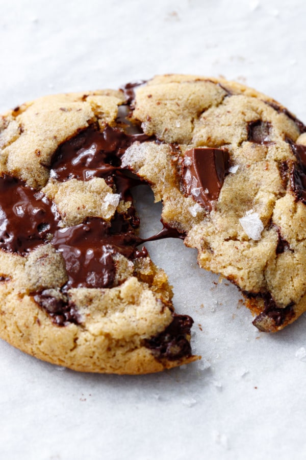 Closeup of olive oil chocolate chip cookie broken in half, with a thread of melted chocolate connecting the two halves.