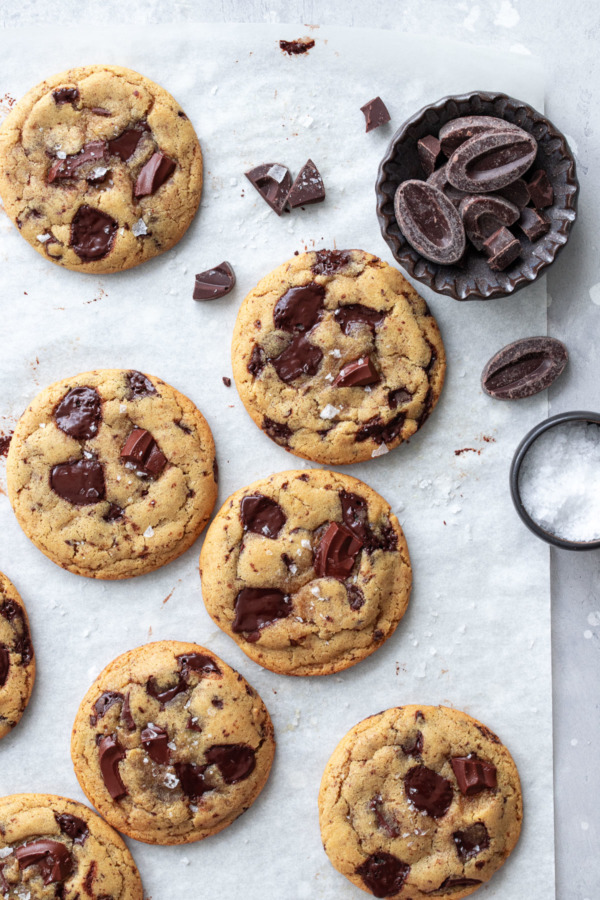 Sur le dessus des cookies aux pépites de chocolat à l'huile d'olive sur parchemin, avec petit bol de morceaux de chocolat et sel de mer en flocons