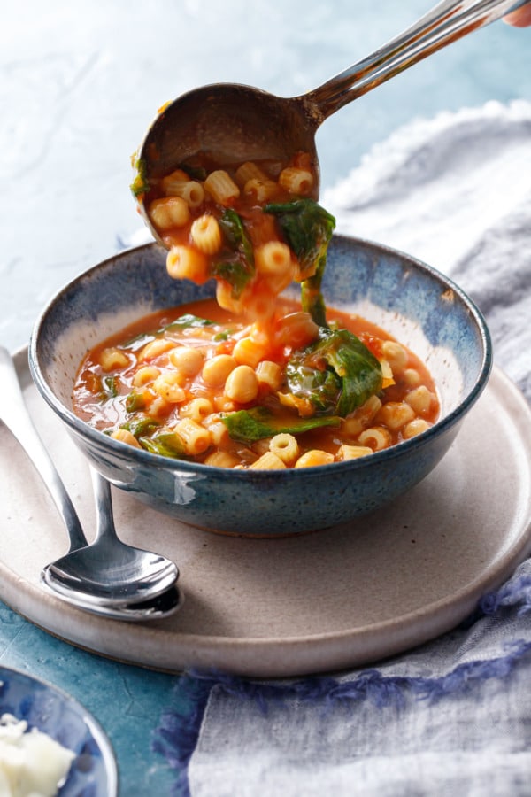 Ladle pouring pasta e ceci stew into a ceramic bowl