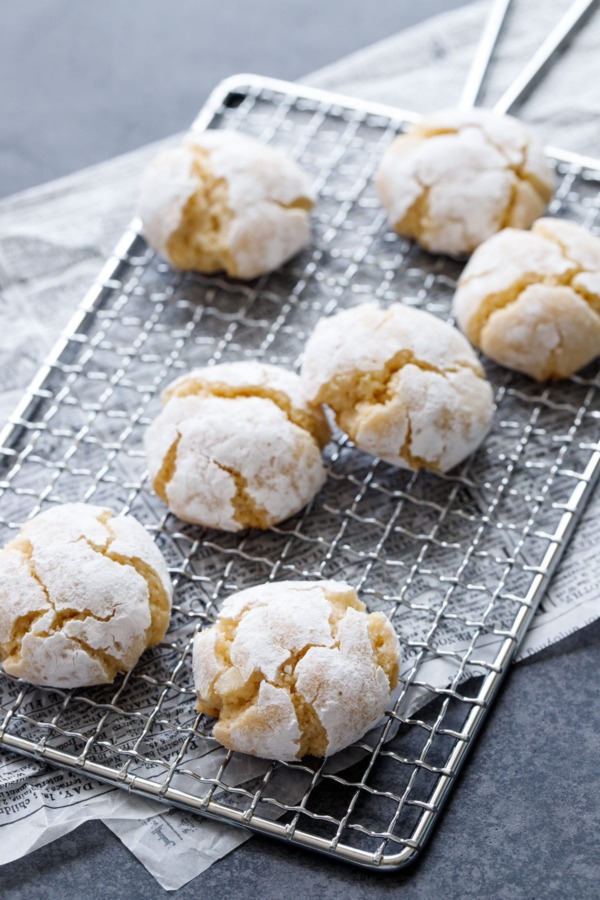 Powdered-sugar coated crinkle cookies on a wire rack, on newsprint parchment on a dark background.