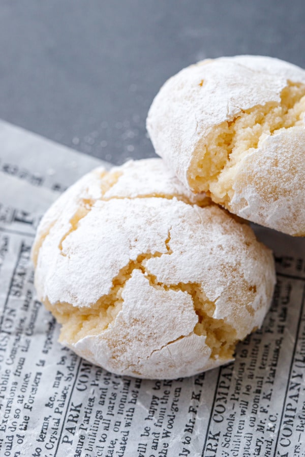 Closeup of two amaretti cookies, coated with powdered sugar with cracks from baking.