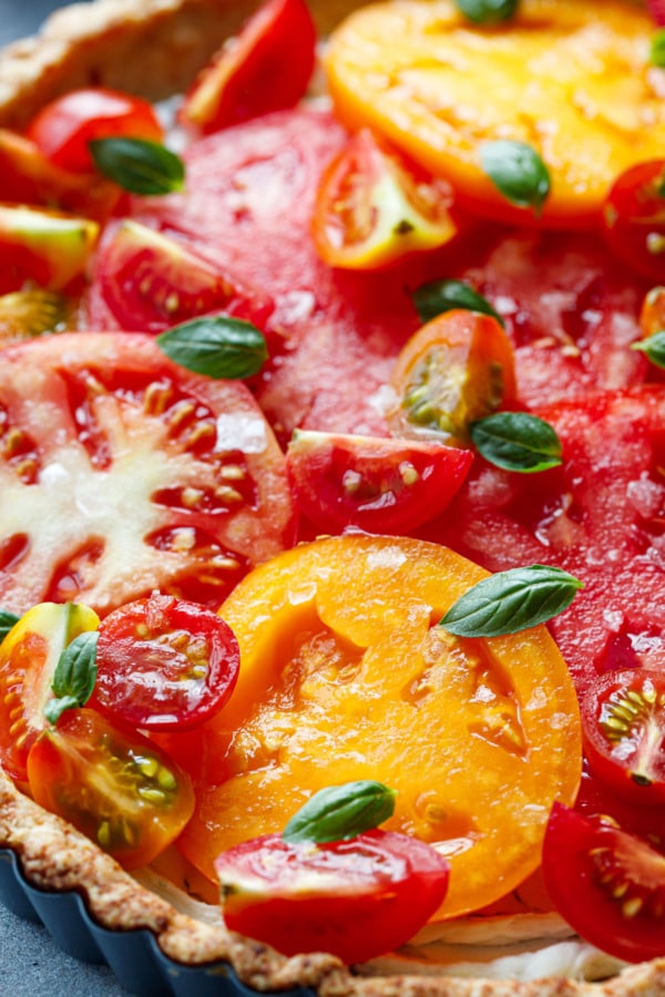 Closeup of heirloom tomato tart topped with tiny basil leaves and flaky sea salt