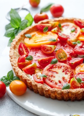 Goat Cheese & Heirloom Tomato Tart on a marble plate surrounded by more tomatoes