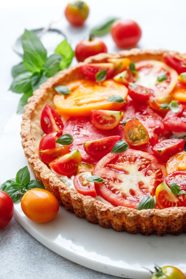 Goat Cheese & Heirloom Tomato Tart on a marble plate surrounded by more tomatoes