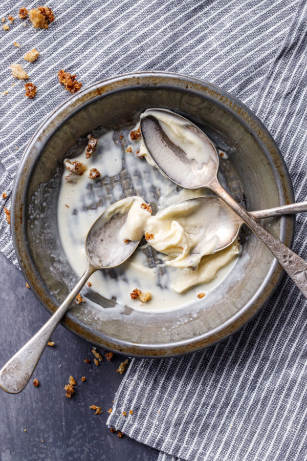 Overhead of a metal tin, three spoons and the remnants of melted and eaten ice cream.