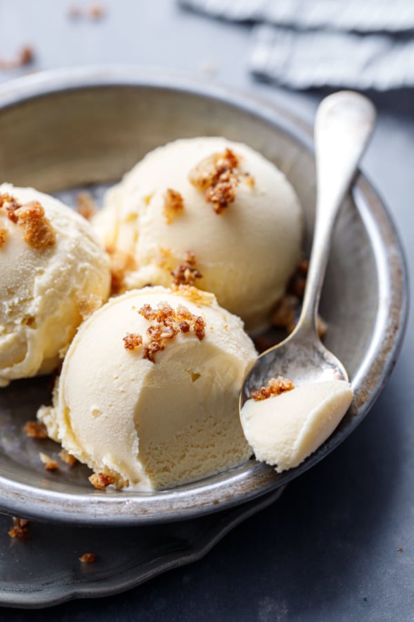 Spoonful of sourdough ice cream, three scoops in a metal pie tin on a gray background.