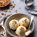 Three scoops of Sourdough Ice Cream in a metal tin, with a spoonful on the site and an old fashioned ice cream scoop in the background.