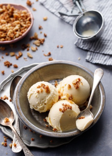 Three scoops of Sourdough Ice Cream in a metal tin, with a spoonful on the site and an old fashioned ice cream scoop in the background.