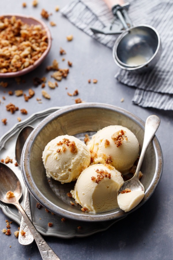 Three scoops of Sourdough Ice Cream in a metal tin, with a spoonful on the site and an old fashioned ice cream scoop in the background.