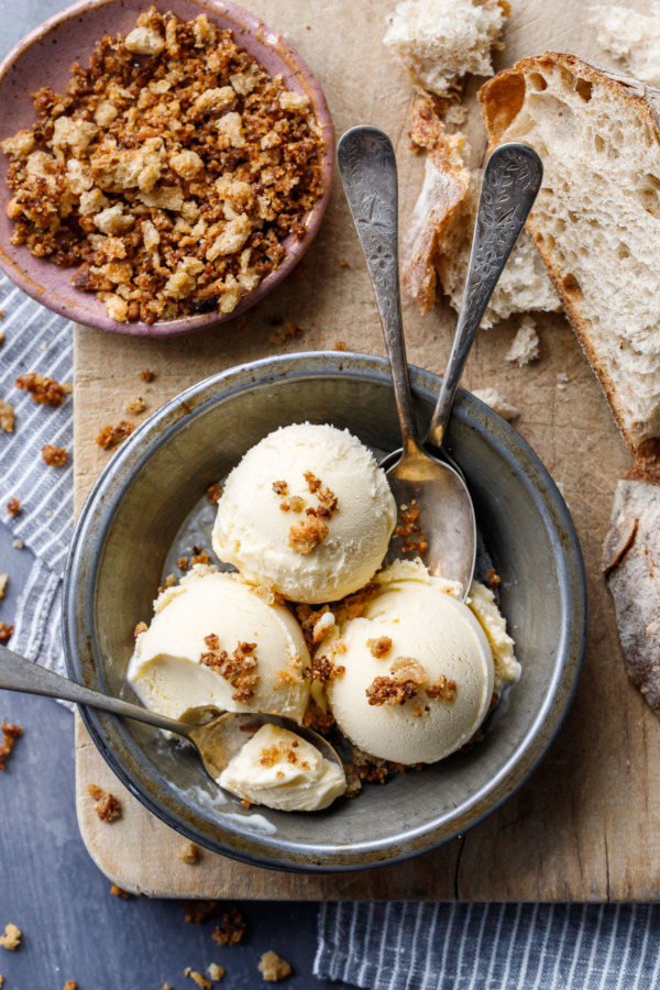 Overhead showing three scoops of Sourdough Ice Cream in a metal tin, with three spoons and a dish of breadcrumbs on the side.