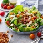 Large shallow dish with butter lettuce and nicoise salad toppings, with a dish of crispy chickpeas and tomatoes and dressing in the background.