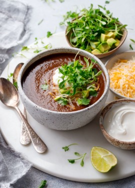 Black bean soup in a bowl with bowls of toppings and spoons on the side.