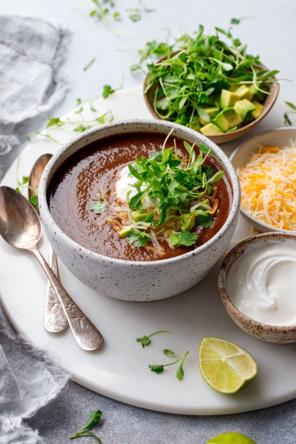 Black bean soup in a bowl with bowls of toppings and spoons on the side.