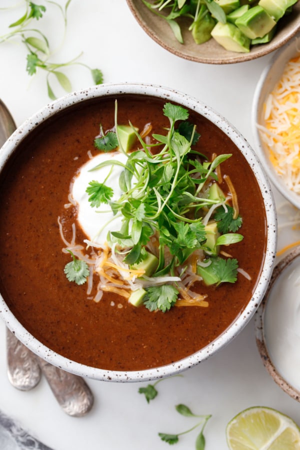 Closeup overhead of black bean soup, topped with cheese, sour cream, and cilantro microgreens