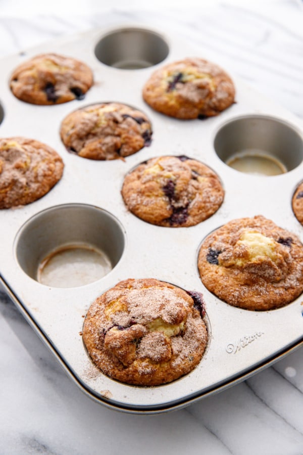 Silver muffin tin with blueberry muffins on a marble background