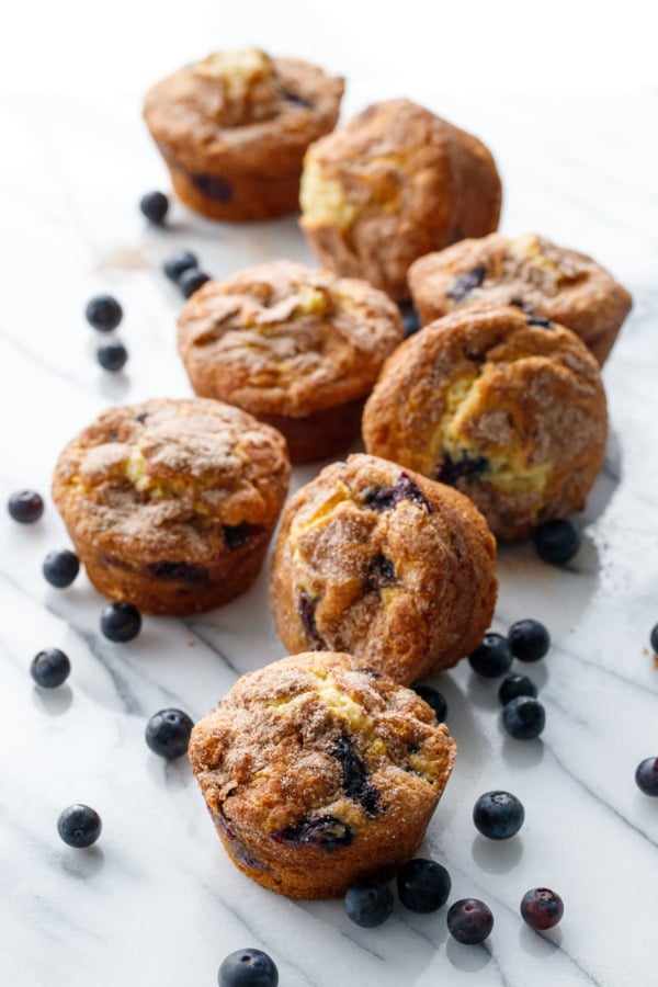 Scattered blueberry muffins and loose blueberries on a marble background