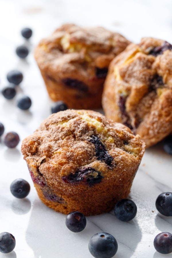 Blueberry muffins on a marble background, with fresh blueberries scattered around.