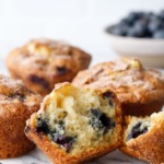 Split blueberry muffin to show inside texture, on marble with more muffins and blueberries in the background