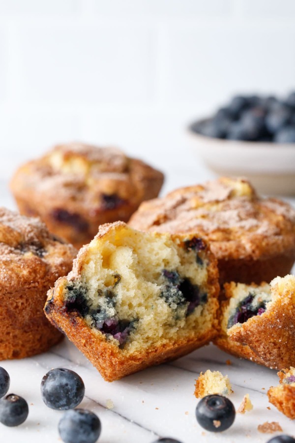 Split blueberry muffin to show inside texture, on marble with more muffins and blueberries in the background