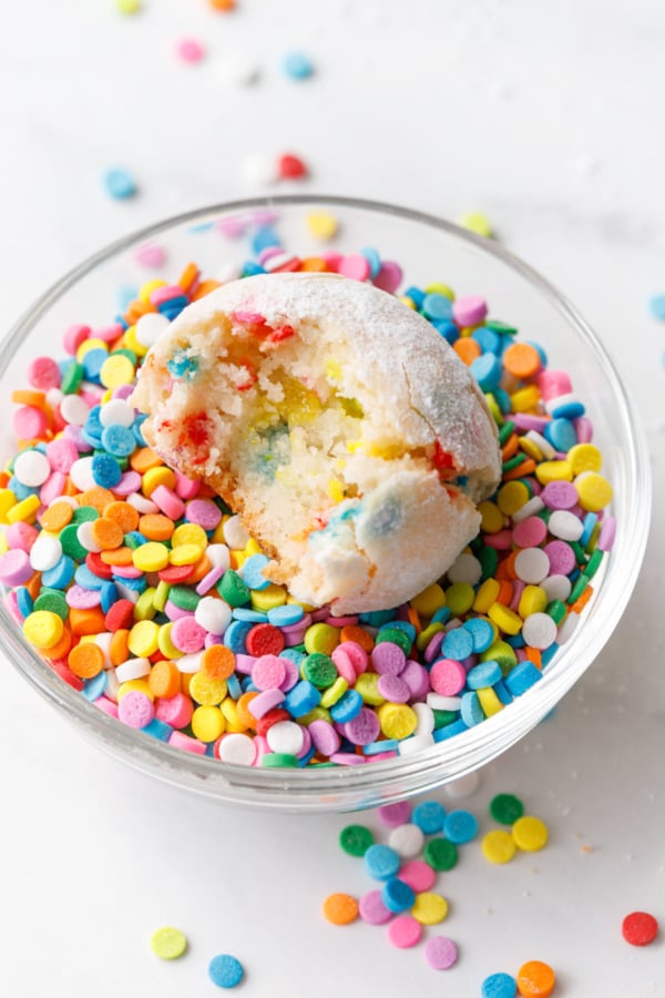 Cookie with a bite out of it sitting in a bowl of rainbow quin sprinkles