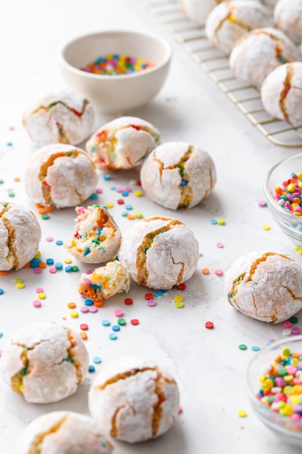 Whole and broken confetti amaretti cookies with a bowl of sprinkles and more scattered around