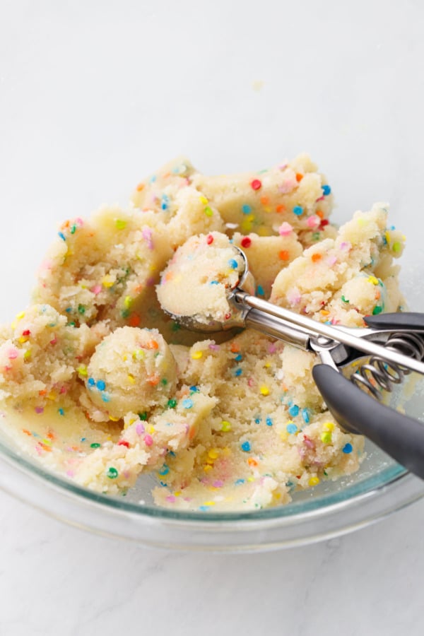 Bowl of amaretti cookie dough with rainbow sprinkles and a cookie scoop