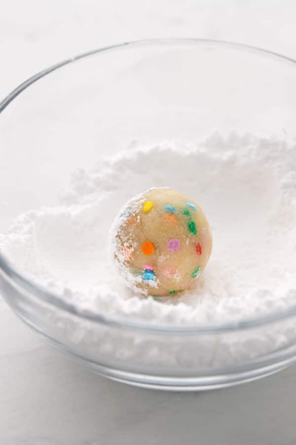 Rolling a ball of confetti amaretti dough in powdered sugar