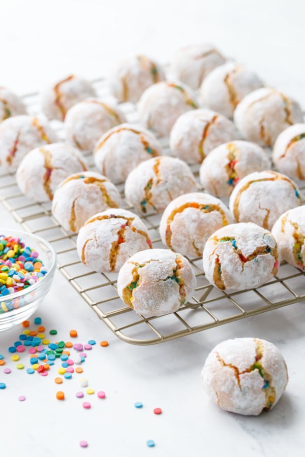 Confetti amaretti cookies on a cooling rack with a bowl of rainbow sprinkles