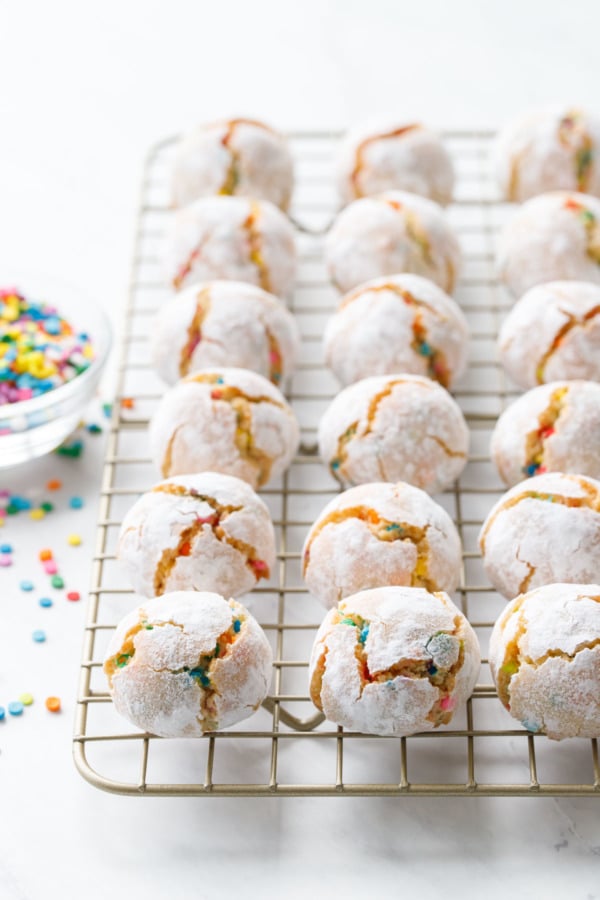 Rows of funfetti amaretti cookies on a cooling rack with a bowl of rainbow sprinkles