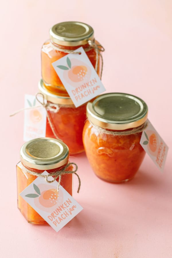 Four jars of orange peach jam in glass jars with hang tags on a pink background