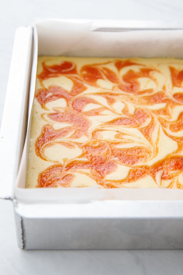 Silver baking pan lined with parchment, baked with cheesecake filling and a bright orange swirl of peach