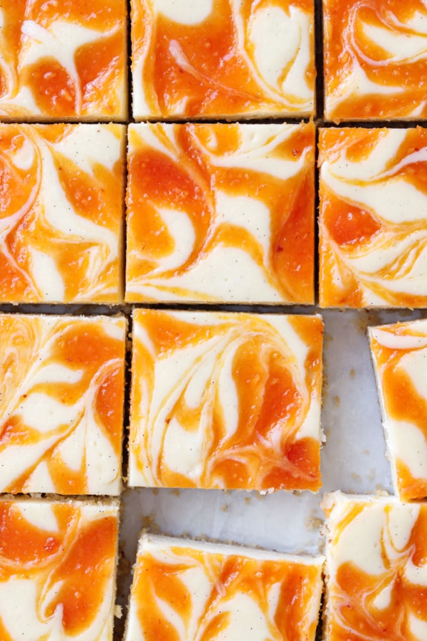 Close up overhead view of sliced peach swirl cheesecake bars, with a few bars slightly offset from grid