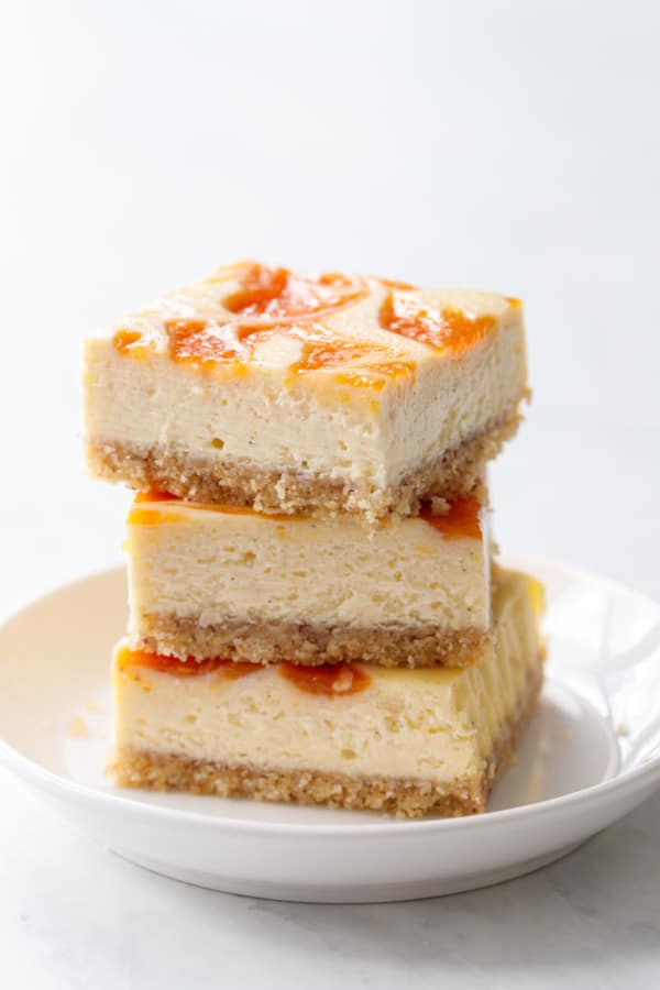 Stack of three squares of peach cheesecake bars, showing the texture of the cheesecake filling and glossy reflection off the swirl of peach baked on top.