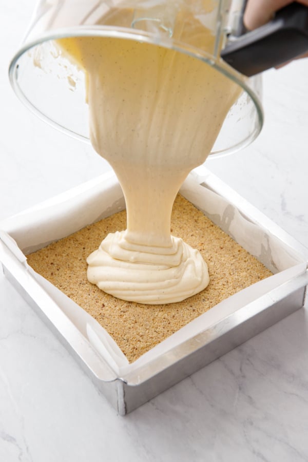 Pouring the cheesecake batter out of the food processor and into the wafer cookie crust.