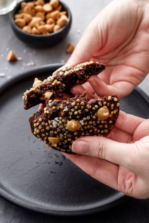 Hands breaking a chocolate cookie in half to show the gooey texture inside