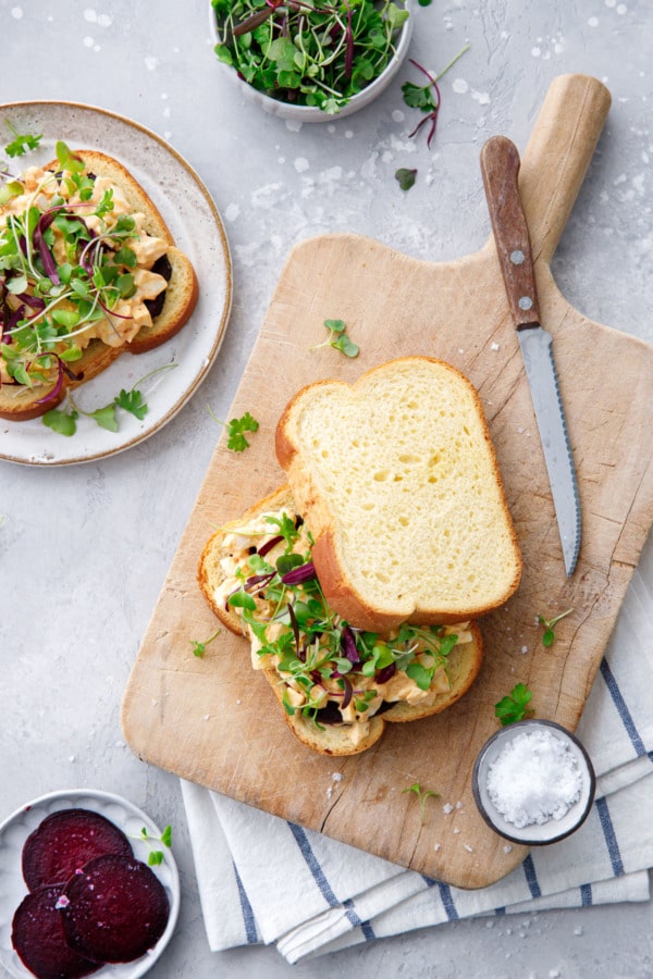 Overhead of egg salad sandwiches with beets and microgreens on a wooden bread board