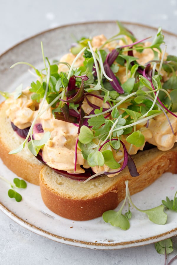 Closeup of open-face egg salad sandwich with beets and microgreens