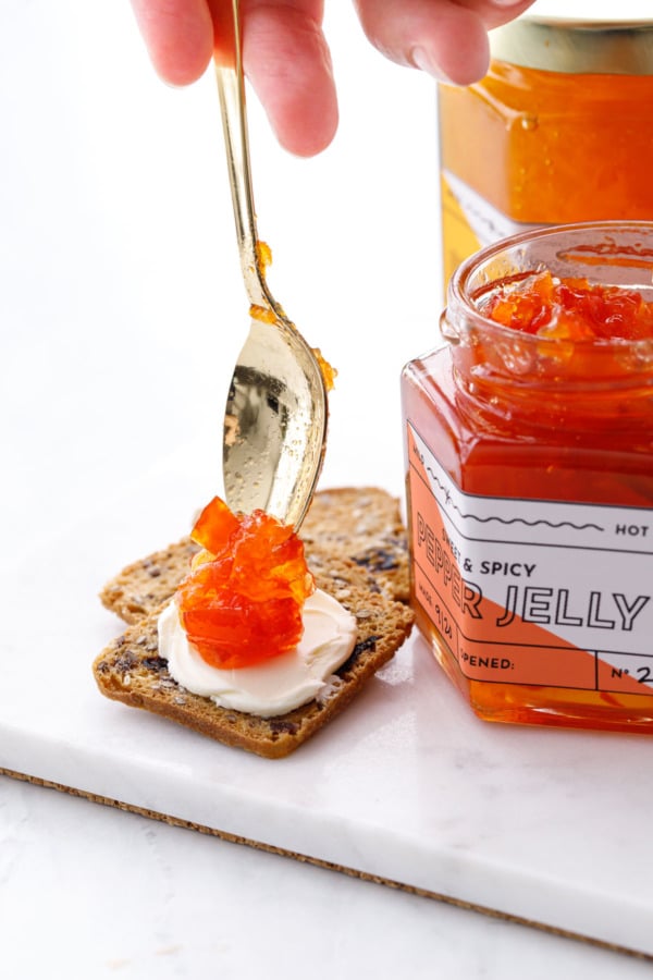 Dolloping a spoonful of red pepper jelly on a cracker with cream cheese