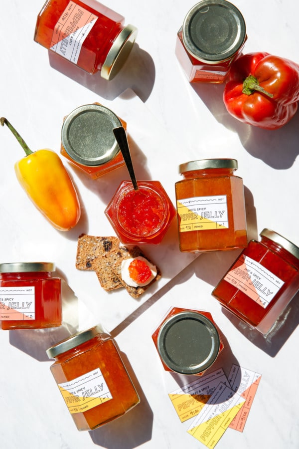 Overhead jars of orange and red pepper jelly with peppers, on marble