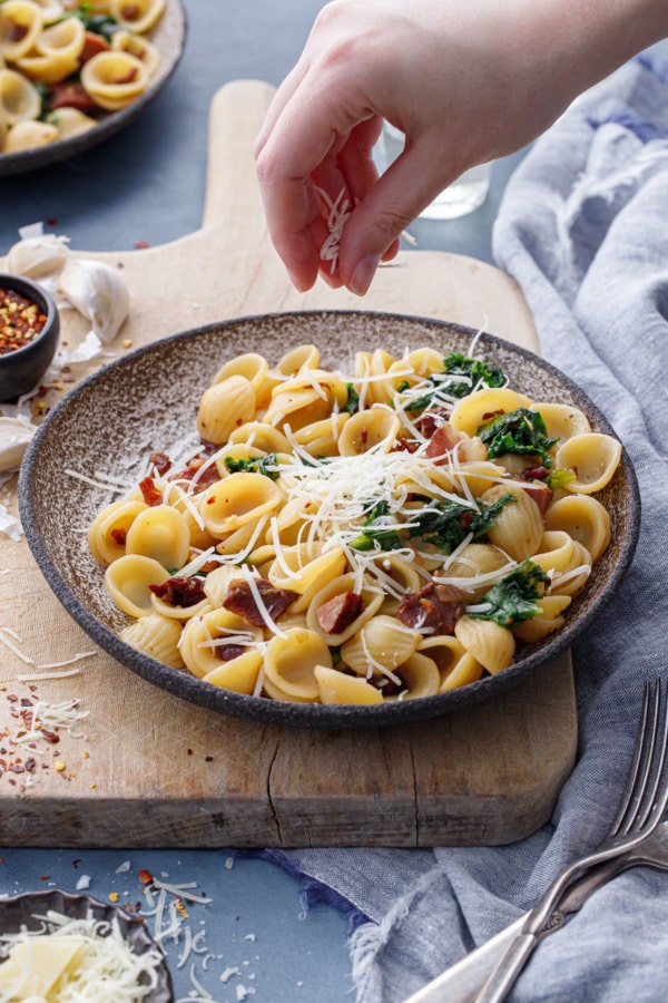 Sprinkling a bowl of orecchiette with pecorino cheese