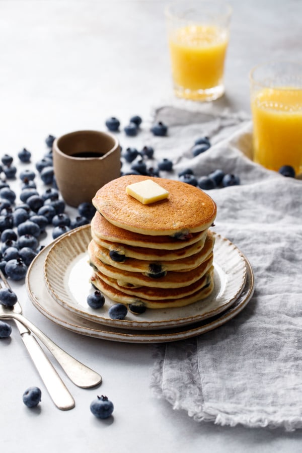 Stack of blueberry pancakes on a ceramic plate, two glasses of orange juice